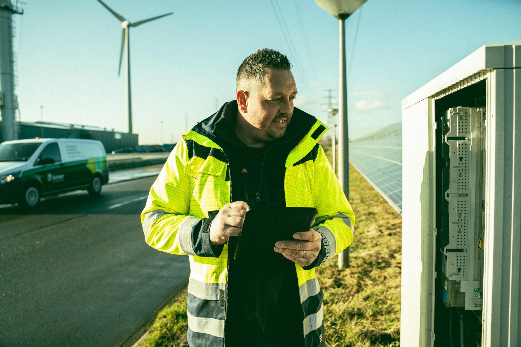 Een medewerker van Kenter staat bij een refurbished transformatorstation en houdt een tablet vast.